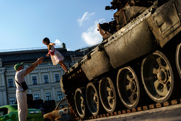 En flicka hoppar ner i sin pappas famn från en rysk stridsvagn, som förstörts och visas upp på ett torg i Kiev.