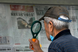 En man använder förstoringsglas för att läsa om Kinas militärövning runt Taiwan under söndagen.