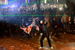 En maskerad demonstrant kastar något mot polisen under protesterna utanför parlamentet i Tbilisi.