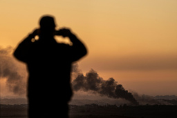 Rök stiger från en explosion i Gazaremsan i måndags. En man i Sderot i Israel följer det på avstånd.