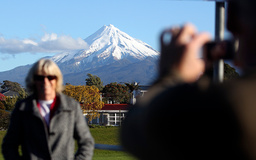 En man fotograferar sin fru med berget Taranaki som fond. Arkivbild.